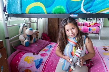 Guadalupe Alvarado im Schlafsaal auf ihrem Bett: Mal keck, mal schüchtern ist die 13jährige, die inmitten von Drogen und Gewalt in einer Wellblechhütte entlang der Bahngleise aufwuchs. Ihre drogenabhängigen Eltern starben früh, ihre Grosseltern schickten sie zum Kaugummi-Verkaufen auf die Strasse statt in die Schule. Vor einem Jahr kam sie freiwillig zu Yolia. Disziplin, Schule, Vertrauen – das sind neue Dinge und grosse Herausforderungen für die 13jährige. Aber Guadalupe will diese Chance auf ein besseres Leben nicht vergeuden.