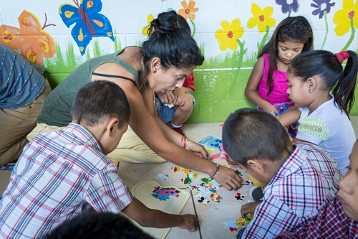 Iris Ophelia Rincán Carías (3.v.links) spielt mit Kindern. Sie bietet in ihrer Freizeit Spielstunden im Kindergarten ihrer Gemeinde in Santa Ana an, um etwas an die Gemeinschaft zurück zu geben. Sie lebt mit ihrer Mutter, die im Rollstuhl sitzt, und ihrer Oma in einem kleinen Haus am Rande von Santa Ana. Ihr Vater verließ die Familie, Geld fehlte. Aber der Frauenhaushalt kämpft. Seit April 2016 studiert Iris dank Adveniat „Englisch“ und will in einem Call Center arbeiten „weil man dort gut verdient“ - vorher hat sie Brot verkauft. Durch das Studium hat sie mehr Selbstvertrauen und ist zum ganzen Stolz der Familie geworden.