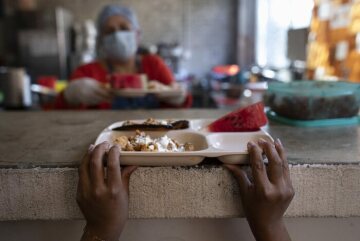 Ein Kind schnappt sich einen Teller mit Essen. Die Migrantenherberge "Casa Mambré" bietet einen sicheres vorübergehendes Zuhause.